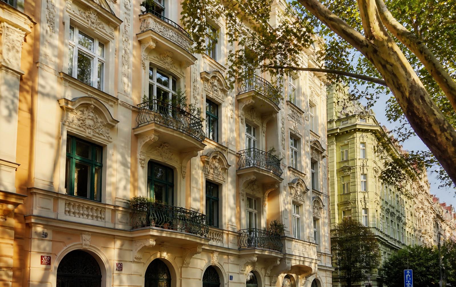 Ornate apartment building facades on a tree-lined Prague street